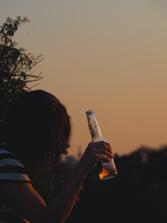 A person standing outside holding a half empty bottle of beer 