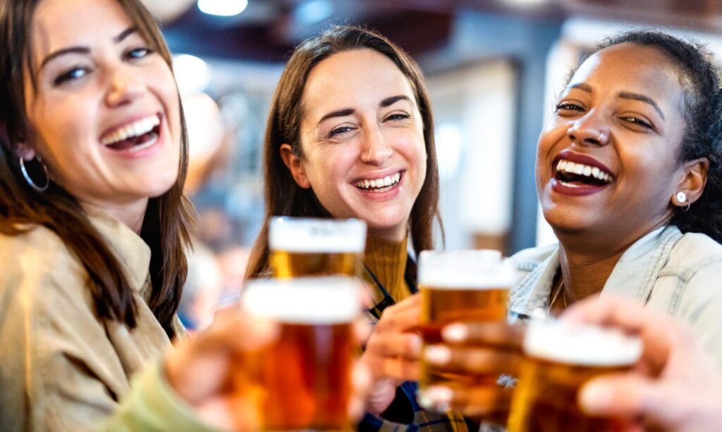 A group of 3 girl smiling and holding glasses of beer