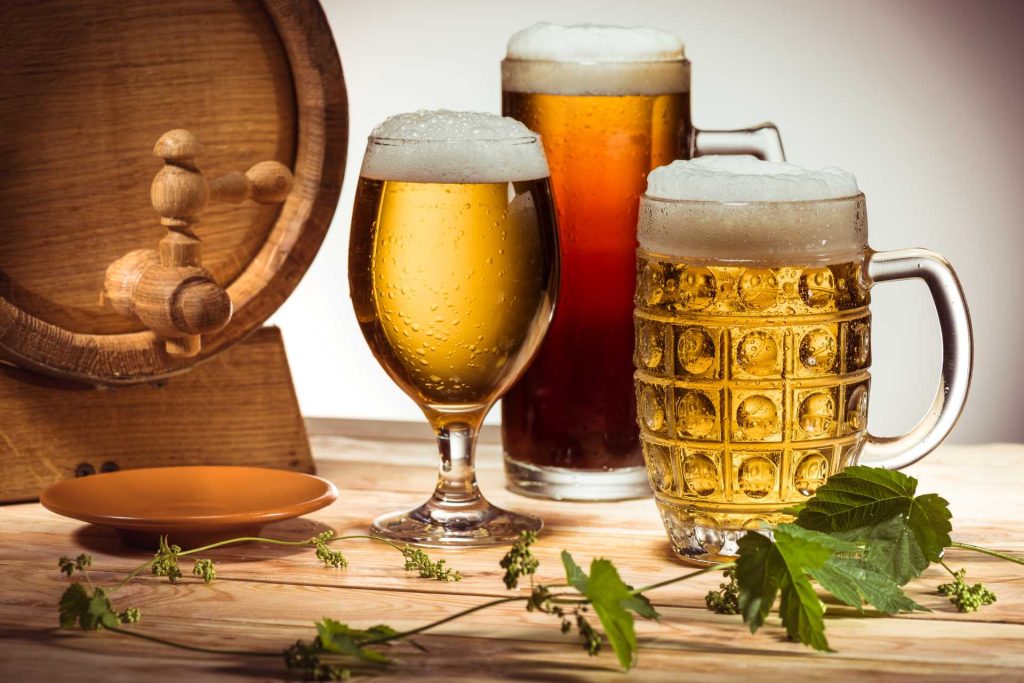 collectible beer mats, barrel and different glasses of beer on wooden tabletop