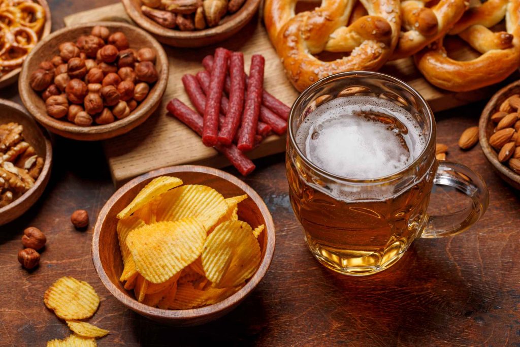 beer tasting party at home, spread of snacks next to glass of beer on wooden surface