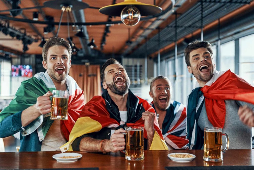 pub olympics games, men cheering at bar with beer wearing different flags